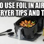 Black air fryer open on a white counter with hot food inside. A roll of foil, tongs, and oil sit next to it. Large text says How To Use Foil In Air Fryer - Air Fryer Tips and Tricks.