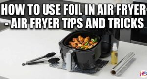 Black air fryer open on a white counter with hot food inside. A roll of foil, tongs, and oil sit next to it. Large text says How To Use Foil In Air Fryer - Air Fryer Tips and Tricks.