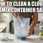 A person cleaning a cloudy Vitamix blender container safely in a bright kitchen using a soft brush, white vinegar, and baking soda.
