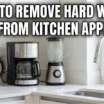 A person scrubbing hard water stains from a cloudy glass pitcher using a small brush and baking soda.
