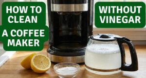 A black drip coffee maker on a wooden kitchen counter next to fresh cut lemons, a small bowl of baking soda, and a glass carafe filled with a bubbly cleaning solution.