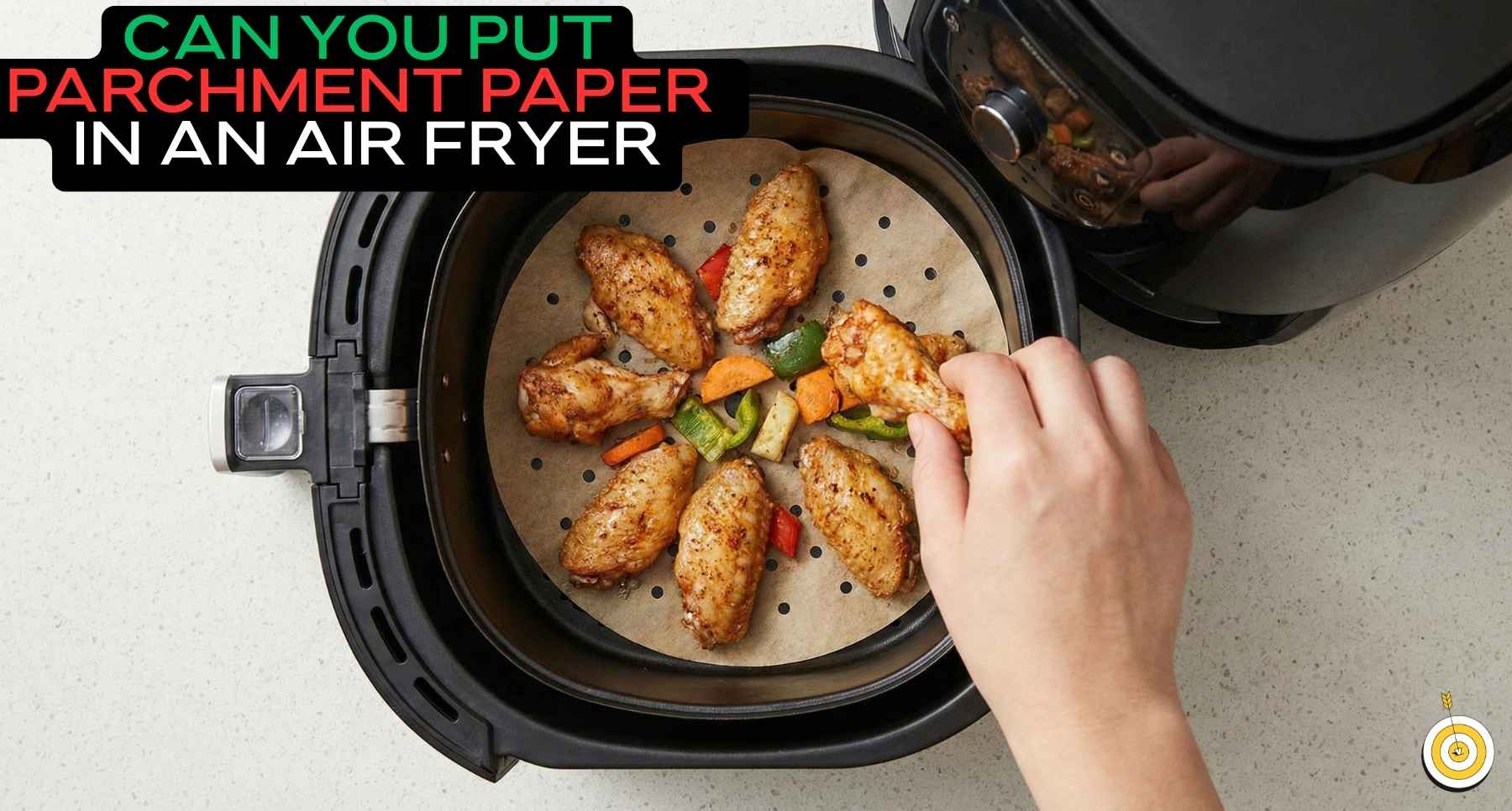 A hand placing seasoned chicken wings and vegetables on perforated parchment paper inside a black air fryer basket.