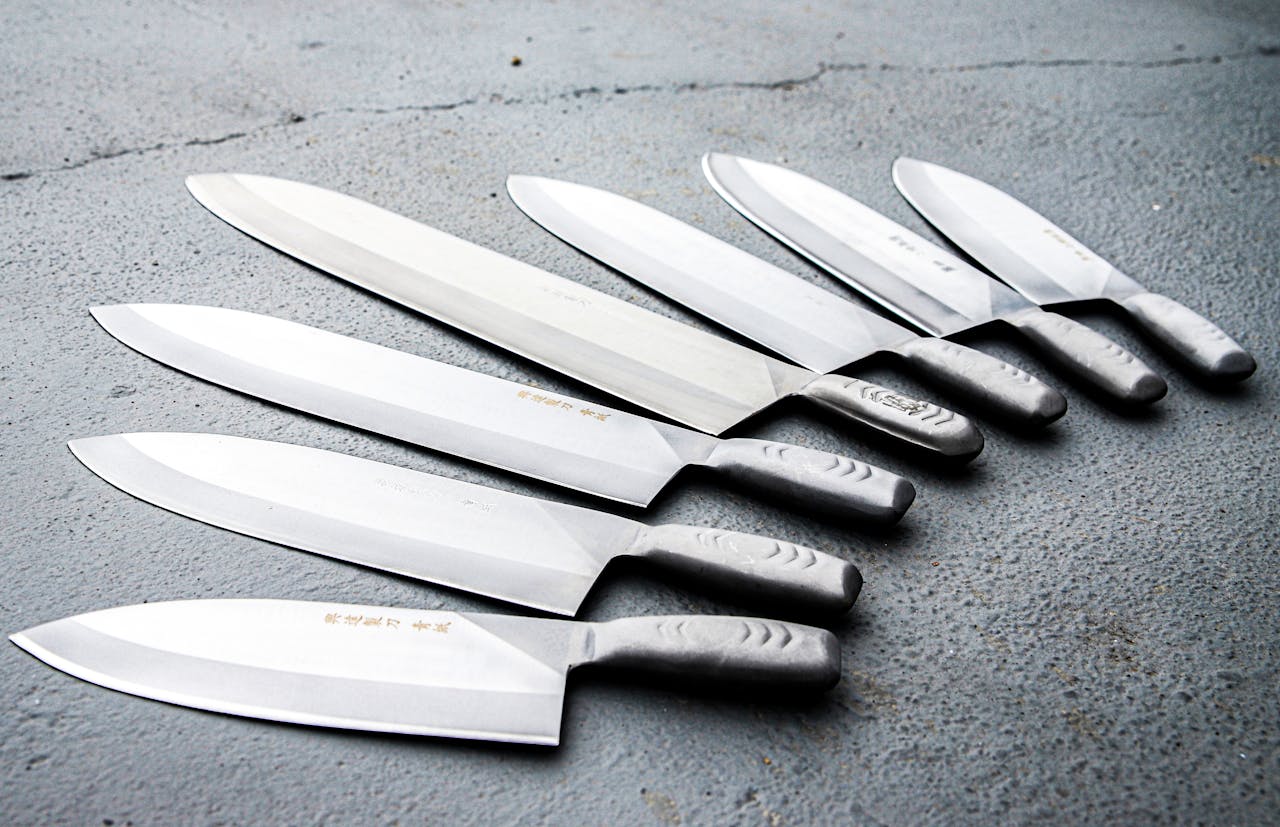 A variety of stainless steel knives neatly arranged on a textured concrete surface, showcasing sharpness and craftsmanship.