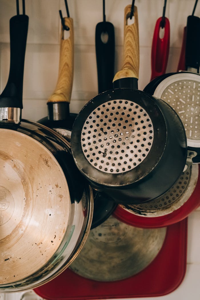 Collection of metal frying pans with wooden and plastic handles hanging on hooks near wall in house