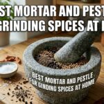 A heavy granite mortar and pestle for grinding spices at home filled with peppercorns and cumin seeds on a wooden kitchen counter.
