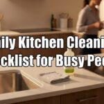 A photograph of a modern kitchen counter with a folded gray cloth and a cleaning spray bottle, featuring large text overlay that reads "Daily Kitchen Cleaning Checklist for Busy People."