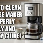 A photograph of a modern stainless steel and black drip coffee maker on a kitchen counter, accompanied by a glass carafe of coffee, a steaming mug, a carton of white vinegar, a bottle of dish soap, and a blue cleaning cloth. Large white text with a black outline overlaid on the left reads: HOW TO CLEAN A COFFEE MAKER PROPERLY (DAILY AND WEEKLY GUIDE).