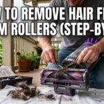 A man sitting on a wooden porch using a seam ripper and tweezers to remove a large amount of tangled pet hair and long hair from a vacuum brush roll.