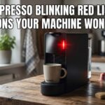 A black Nespresso machine on a wooden kitchen counter with a glowing red light and the text Nespresso Blinking Red Light: 9 Reasons Your Machine Won’t Brew.