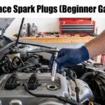 A person wearing blue gloves uses a ratchet and extension bar to install a new spark plug into a car engine.