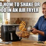 A smiling man in a bright kitchen tossing golden french fries in a wire basket next to a black air fryer. Large text reads: When and How to Shake or Flip Food in an Air Fryer.