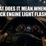 Driver gripping a steering wheel at night with a bright check engine light flashing on the dashboard.