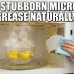 A hand wipes a clean path through stubborn orange grease inside a microwave. A bowl of steaming lemon water sits on the turntable. Bold white text says: CLEAN STUBBORN MICROWAVE GREASE NATURALLY!