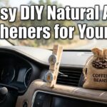 Natural car air freshener display on a dashboard featuring a DIY wooden vent clip, a burlap coffee bean pouch, and peppermint essential oil.