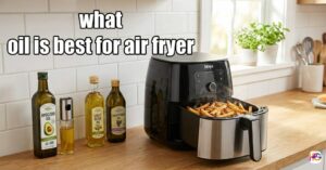 A black air fryer with an open basket full of crispy french fries on a kitchen counter next to bottles of avocado oil, light olive oil, grapeseed oil, and an oil sprayer, with the text what oil is best for air fryer.
