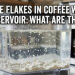 Close-up of a clear coffee maker water reservoir filled with chalky white flakes and mineral deposits.