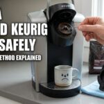 A hand uses a metal paperclip to clean a clogged Keurig needle.