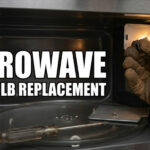 A person wearing a brown work glove replaces a small light bulb inside a microwave oven with a screwdriver resting on the glass turntable.