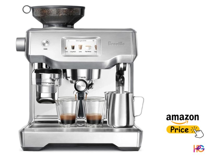 A close-up, front-facing view of a silver Breville Oracle Touch espresso machine on a white background. A bean hopper is full of whole beans, and the machine has extracted dark espresso into two small clear glasses beneath the dual spout. A stainless steel milk pitcher is on the right. The color touchscreen display shows a 'Select your drink' menu with various icons.