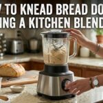 An image of a countertop blender vigorously kneading a ball of bread dough. Text overlay at the top reads: 'HOW TO KNEAD BREAD DOUGH USING A KITCHEN BLENDER'. A woman's hands are visible operating the machine.