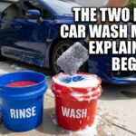 An outdoor shot of a blue car in a driveway with two buckets—a blue "RINSE" bucket and a red "WASH" bucket—featuring a gray wash mitt and text overlay that reads "THE TWO BUCKET CAR WASH METHOD EXPLAINED FOR BEGINNERS".