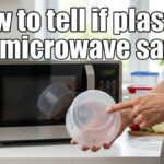 A person wearing a grey apron holds a clear plastic container and points to the microwave-safe icon and #5 PP recycling symbol on the bottom. A modern microwave and a stack of colorful food containers are visible on the kitchen counter in the background.