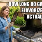 An American woman in a backyard holding up a severely rusted and degraded metal gas grill flavorizer bar next to an open stainless steel barbecue grill.