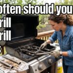 An American woman on a wooden backyard deck cleaning the stainless steel burner tubes of an open gas grill using a wire brush.