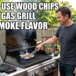 An American man on a wooden deck uses tongs to place an aluminum foil pouch filled with wood chips onto a gas grill to create smoke flavor.