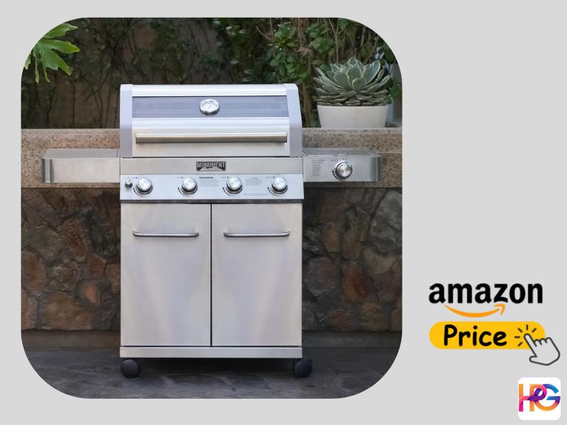 A stainless steel Monument 4-burner natural gas grill with a side burner sitting on a patio in front of a stone wall, featuring an Amazon Price button on the right side.