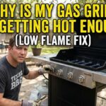 A man in a Texas BBQ t-shirt troubleshooting a gas grill in a backyard with text overlay "Why is my gas grill not getting hot enough? (Low flame fix)".