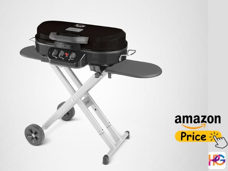A black Coleman RoadTrip 285 portable gas grill is shown on its silver, collapsible, wheeled X-stand with both grey side tables extended. It has three control knobs and a lid latch. An 'Amazon Price' graphic with a hand icon is on the bottom right.