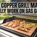 A photograph of an open, outdoor gas grill with a large, flat copper-colored grilling mat sitting directly on top of the metal grates. The mat creates a continuous, non-stick cooking surface over the heat, while the grill itself is clean. White, distressed text over the open lid reads, "DO COPPER GRILL MATS ACTUALLY WORK ON GAS GRILLS?"