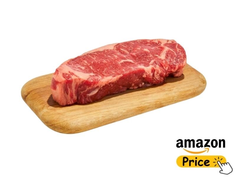 A thick, raw beef New York strip steak with visible fat marbling resting on a small, light-colored wooden cutting board over a white background.